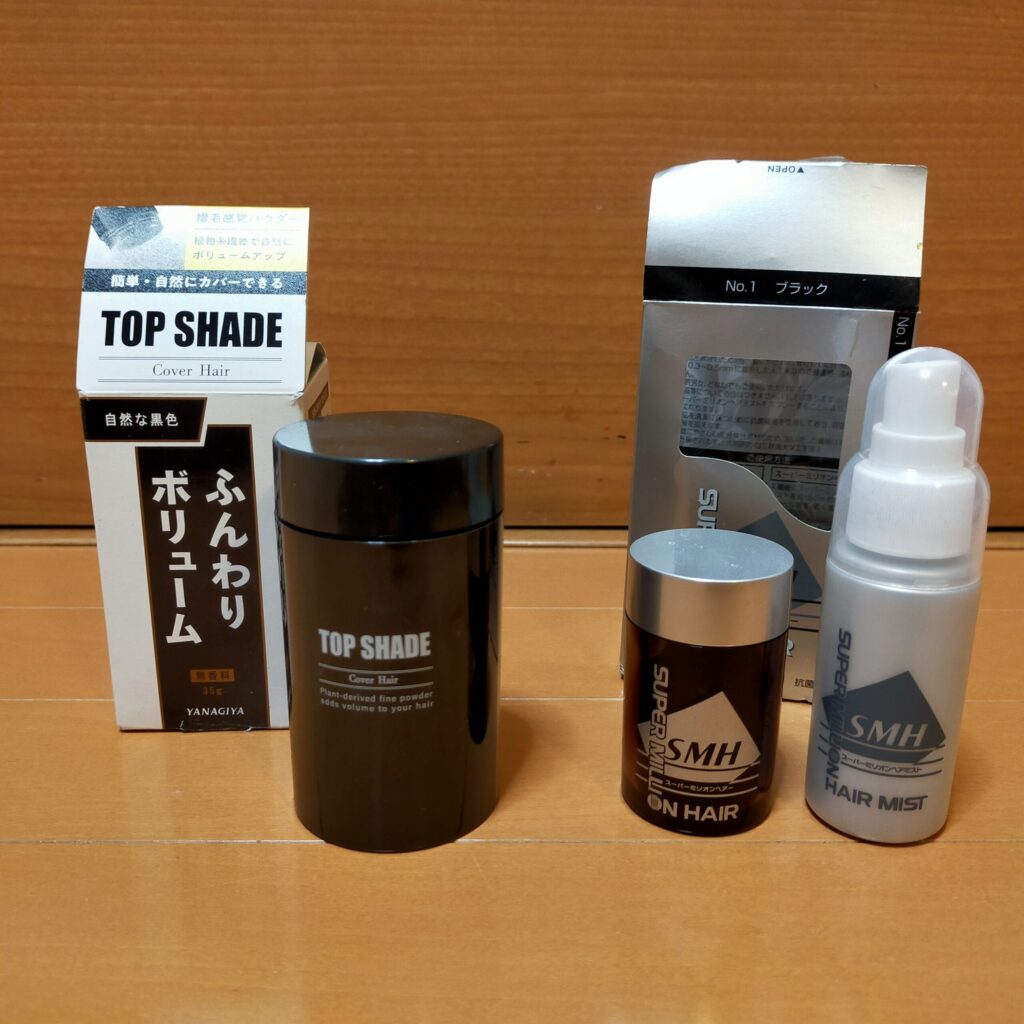 増毛パウダー2製品の比較写真。左に柳屋トップシェード(箱と容器)、右にスーパーミリオンヘアーのパウダー容器とヘアミストボトルを並べて撮影。